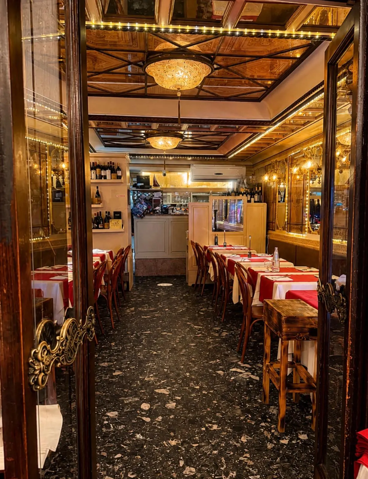 Historic indoor dining room with gilded mirrors, Murano chandeliers and red-linen tables